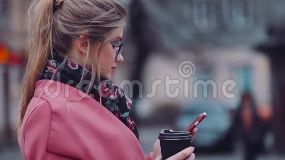 旋转观看一个华丽时尚的女孩拿着一杯咖啡用她的手机上网商务视频的预览图