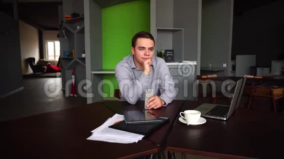 成功的年轻男性商人的画像他们手拿着智能手机摆姿势看着远方坐在办公桌前视频的预览图