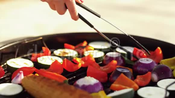 有钳子的女人在烧烤架上煮蔬菜视频的预览图