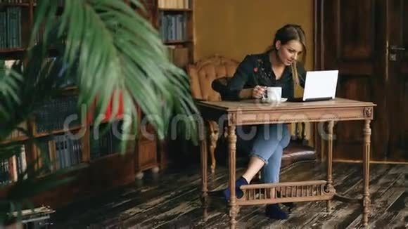 微笑的学生女孩工作笔记本电脑和喝咖啡在大学图书馆室内视频的预览图