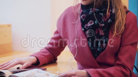 近距离观看一本时尚的年轻女孩翻转杂志然后她戴上耳机享受音乐快乐视频的预览图