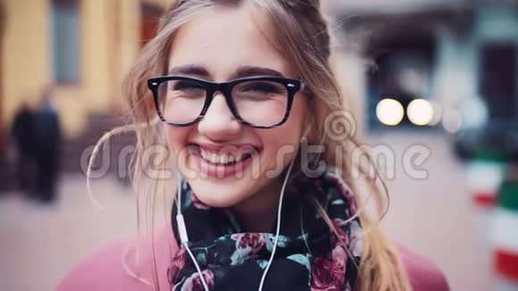 特写一个年轻可爱的女孩戴着耳机迷人地微笑着朝相机走去随意的发型美丽美丽视频的预览图