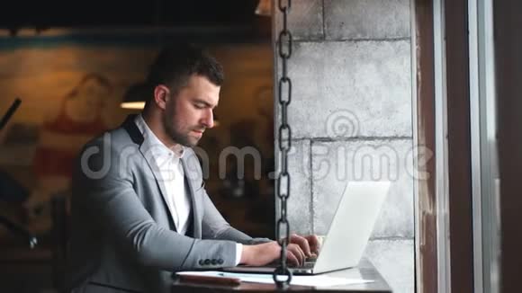 一个留着胡子的男人企业家坐在咖啡馆里做远程工作时拿着笔记本电脑视频的预览图