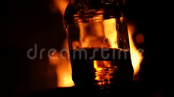 啤酒瓶在黑暗中的火背景上棕色玻璃上的火焰游戏慢动作视频的预览图