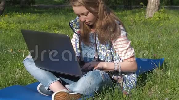 一个青少年正在大自然中的笔记本电脑上打字那个女孩坐在公园的地毯上一个十几岁的女孩在阳光明媚的日子和洛杉矶视频的预览图