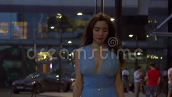 美丽的黑发女孩穿着蓝色连衣裙晚上在街上散步4K剪辑视频的预览图