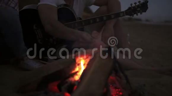 海滩大火中烤香肠的特写镜头一群年轻快乐的人坐在海边的火炉旁视频的预览图