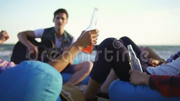一群朋友喝着鸡尾酒和啤酒坐在沙滩上的安乐椅上听着一首歌视频的预览图