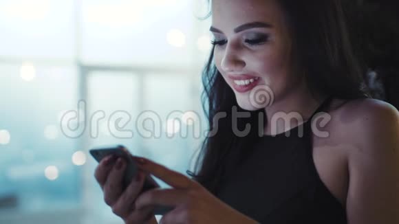 近距离观看迷人的年轻女性穿着时尚的黑色上衣上网在明亮的灯光下微笑视频的预览图