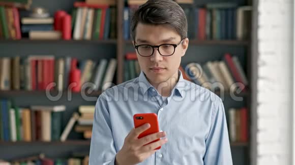 年轻人用智能手机画像笑站在图书馆社交媒体上搞笑视频的预览图