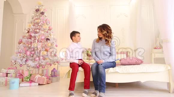 专心致志的儿子在节日前夕在明亮的卧室里送给母亲圣诞礼物里面有节日的圣诞树和礼物视频的预览图