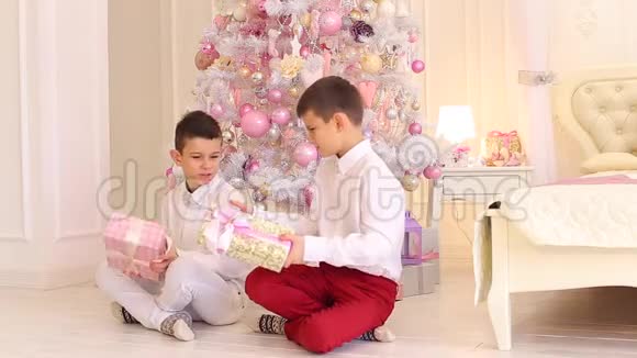 可爱的男孩兄弟学习礼物坐在卧室的地板上与圣诞树视频的预览图
