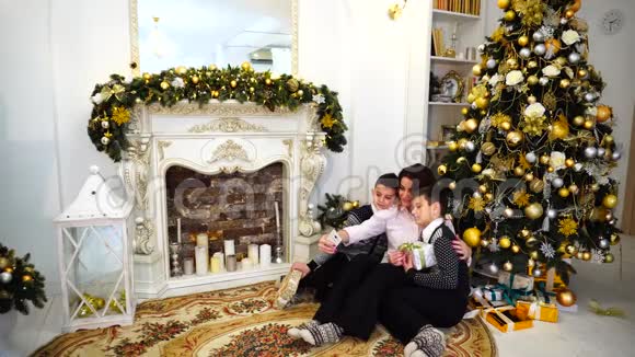 迷人的女人两个男孩的母亲和孩子们一起在智能手机上自拍坐在客厅的地板上视频的预览图