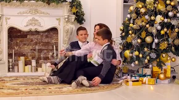 漂亮的女性两个儿子的母亲用双胞胎在智能手机上自拍坐在客厅的地板上装饰视频的预览图