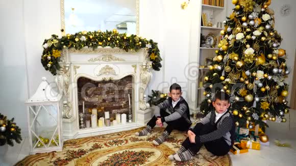 两个可爱的孩子和弟弟在客厅的圣诞树下坐着相机聊天和摆姿势视频的预览图
