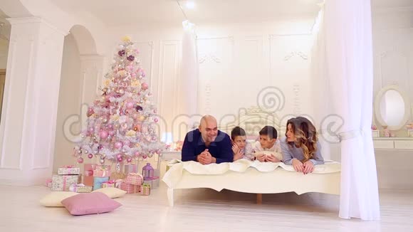 大家庭交流爸爸妈妈和他们的小儿子玩得开心躺在明亮的卧室的大床上视频的预览图