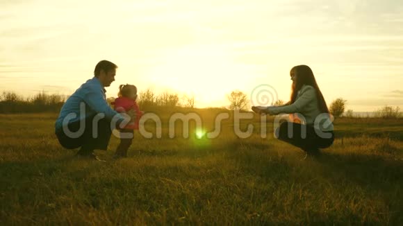 宝宝从爸爸到妈妈都在草坪上孩子在公园里迈出第一步爸爸妈妈和孩子在日落时在草地上玩视频的预览图
