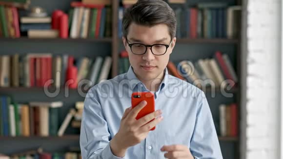 年轻人用智能手机画像笑站在图书馆社交媒体上搞笑视频的预览图