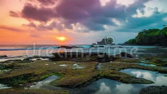 在破碎的海滩上日落时间在远处人们可以看到巴厘岛的塔纳罗特神庙视频的预览图