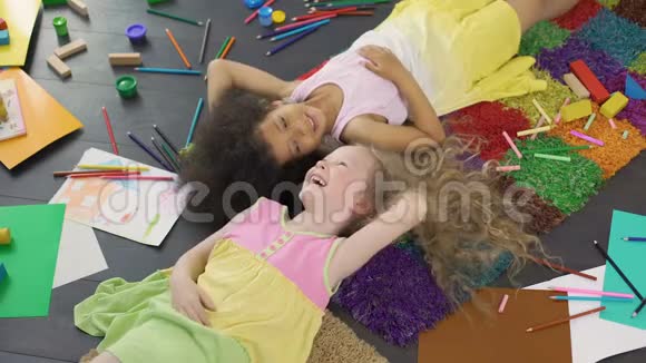 两个多种族的女孩子躺在地毯上笑着快乐的童年视频的预览图