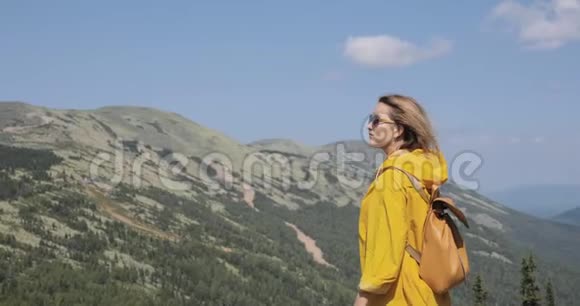 年轻女子穿着黄色雨衣在山上徒步旅行视频的预览图