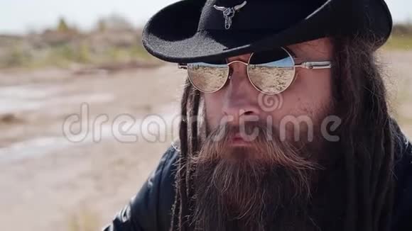 一个戴着黑帽子戴着胡子的眼镜的酷牛仔在沙漠中眺望远方视频的预览图