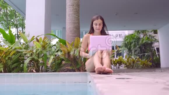 女人坐在游泳池旁把笔记本电脑扔进水里那个女孩正在靠一台小型电脑选择性聚焦视频的预览图