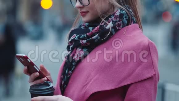 现代时尚女孩端着一杯咖啡用手机上网然后看着相机分享视频的预览图