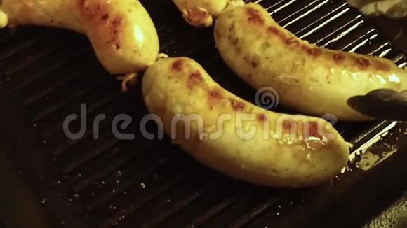 在黑色煎锅上用烤架特写香肠半成品用火钳煎翻慢慢视频的预览图