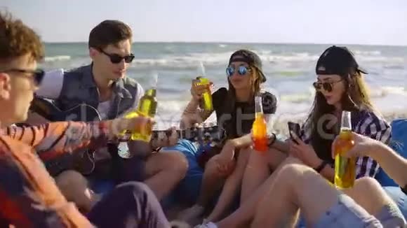 一群朋友喝着鸡尾酒和啤酒坐在沙滩上的安乐椅上听着一首歌视频的预览图
