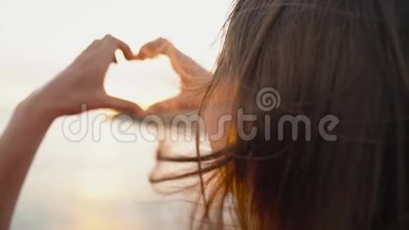 在海滩上日落的时候女人用她的手做心的象征慢动作视频的预览图