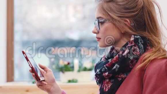 漂亮的金发女孩坐在中央咖啡馆里用手机发信息模糊图像女性肖像视频的预览图