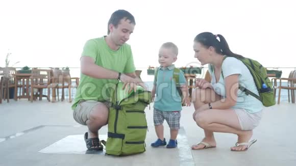 父母从背包里拿出一个婴儿壶放一个儿子在上面在海边的餐馆里的家人视频的预览图