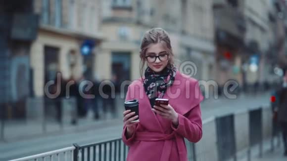 穿着优雅服装的漂亮女孩端着一杯咖啡走在拥挤的街道上用她视频的预览图