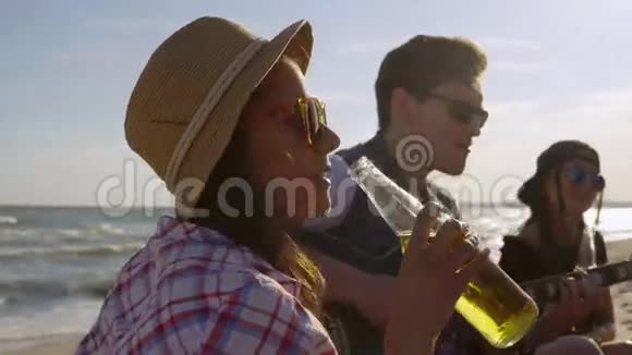 年轻快乐的朋友喝着啤酒坐在沙滩上的安乐椅上听着一个朋友弹吉他视频的预览图