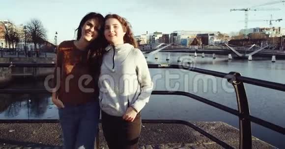 两个年轻女孩看着相机微笑的肖像两个可爱的女孩坐在城市街道上户外晴天视频的预览图