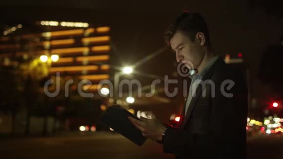 年轻的游客晚上在街上使用他的平板电脑视频的预览图