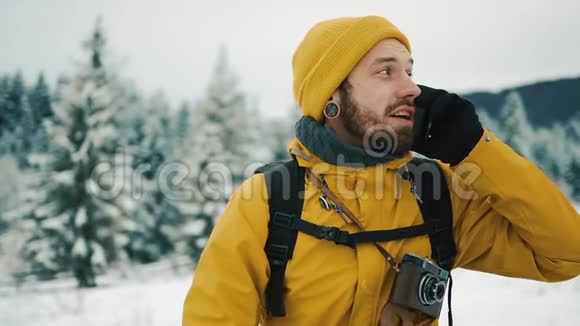 有胡子的人穿着黄色的冬衣在电话里说话一个徒步旅行者带着背包去冬山视频的预览图