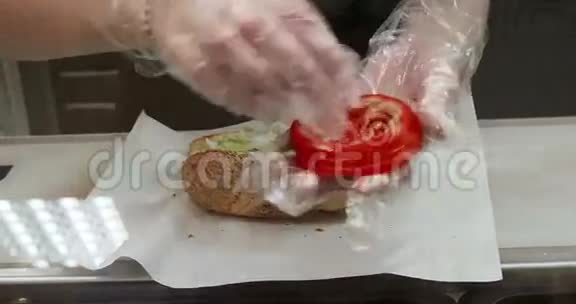戴着透明手套的女人在当地的快餐纸上准备三明治在开放的面包里加入新鲜蔬菜视频的预览图