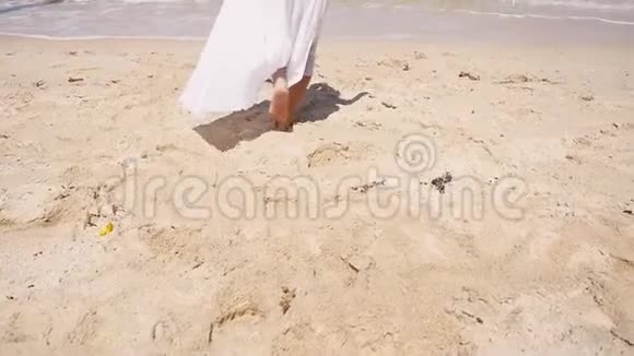 快乐的年轻女子穿着白色的连衣裙和花圈光着脚跑到海里高兴地举手海滩视频的预览图