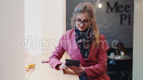 可爱的小女孩穿着休闲装坐在咖啡馆里用她的平板电脑上网看着视频的预览图