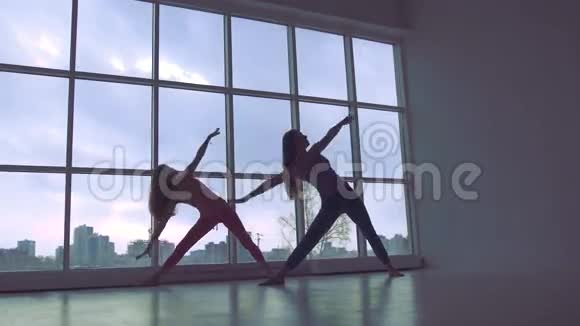 两个可爱的瑜伽女人一起在大窗户的工作室做瑜伽视频的预览图