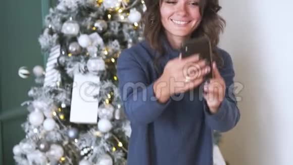 在圣诞树的背景下用手机拍下迷人的深色头发的自拍视频的预览图