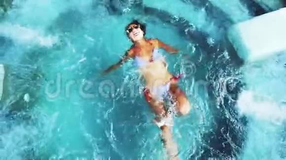俯瞰美丽的棕色年轻女子比基尼和太阳镜享受豪华水疗治疗水射流游泳池慢慢慢慢视频的预览图
