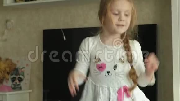 小女孩手里拿着手机耳机跳着在房间的沙发上跳舞视频的预览图