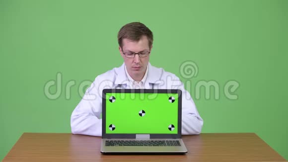 男医生坐着展示彩色钥匙绿色屏幕笔记本电脑视频的预览图