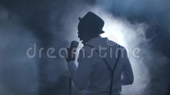 男歌手的视线从后面的烟雾和白光唱成麦克风和舞蹈黑色背景视频的预览图