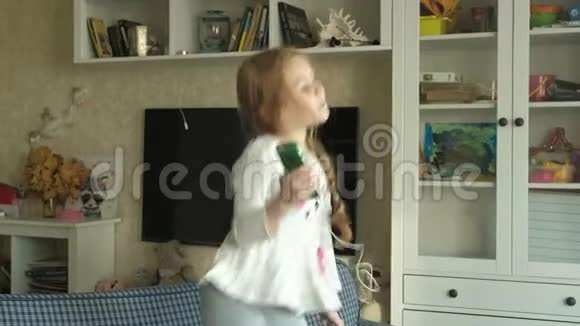 小女孩手里拿着手机耳机跳着在房间的沙发上跳舞视频的预览图