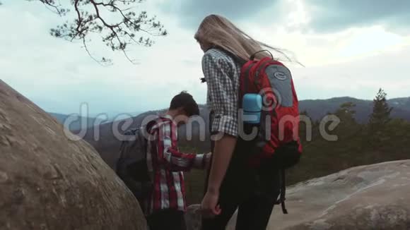 一对年轻夫妇爬上岩石山一个带背包的时髦小伙子带着一个漂亮的女朋友向他伸出了手视频的预览图