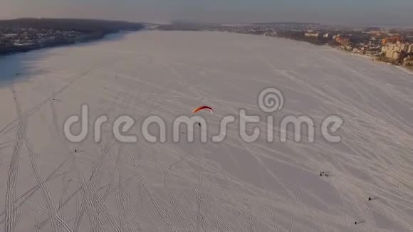 空中观景当天日落时分在城市公园附近的一个冰冻湖上滑翔伞飞行员的比赛视频的预览图